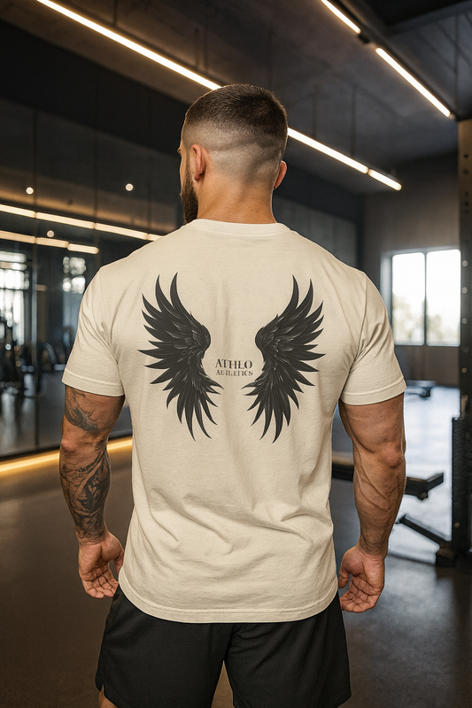 Man wearing a beige t-shirt with black wing design and 'ATHLO' branding in an indoor setting.